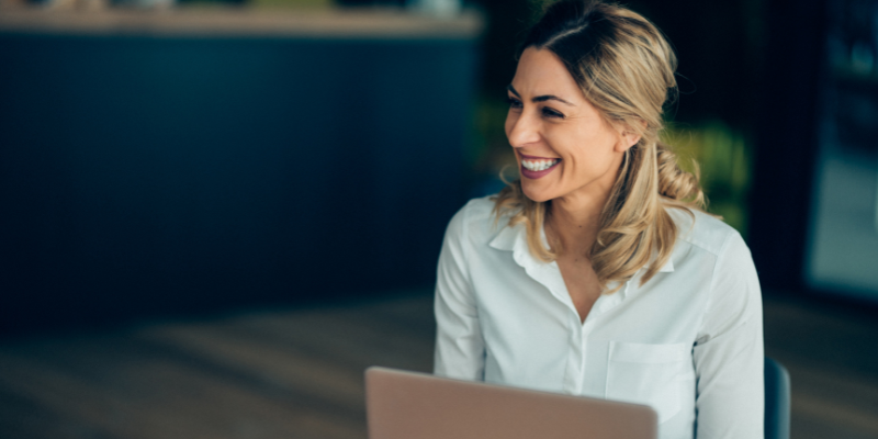 A woman with a laptop smiling, student of the global executive mba in a business school